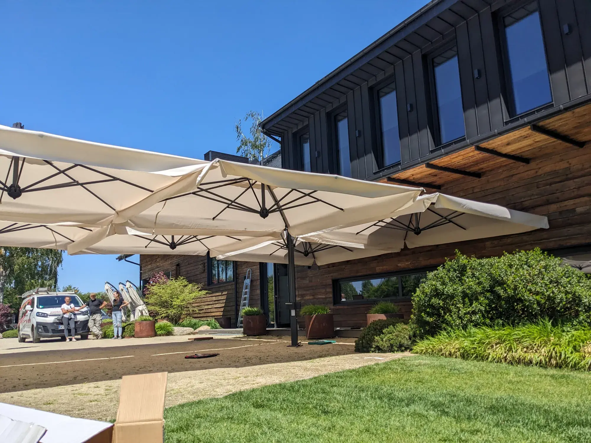 Alu Poker 6×6 m parasols in front of the Karma House guesthouse with its dark wood facade
