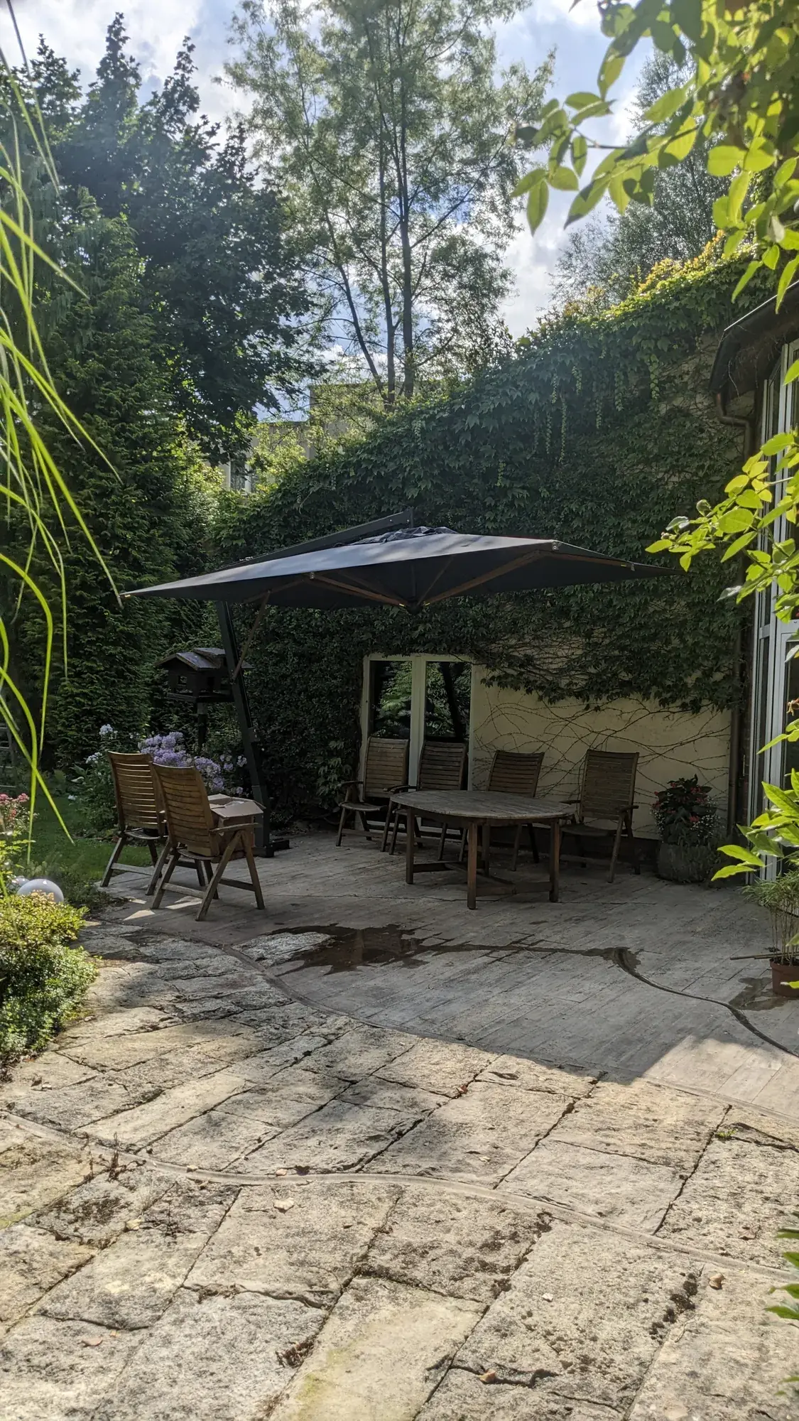 Parasol with a dark canopy over a table on a stone garden patio