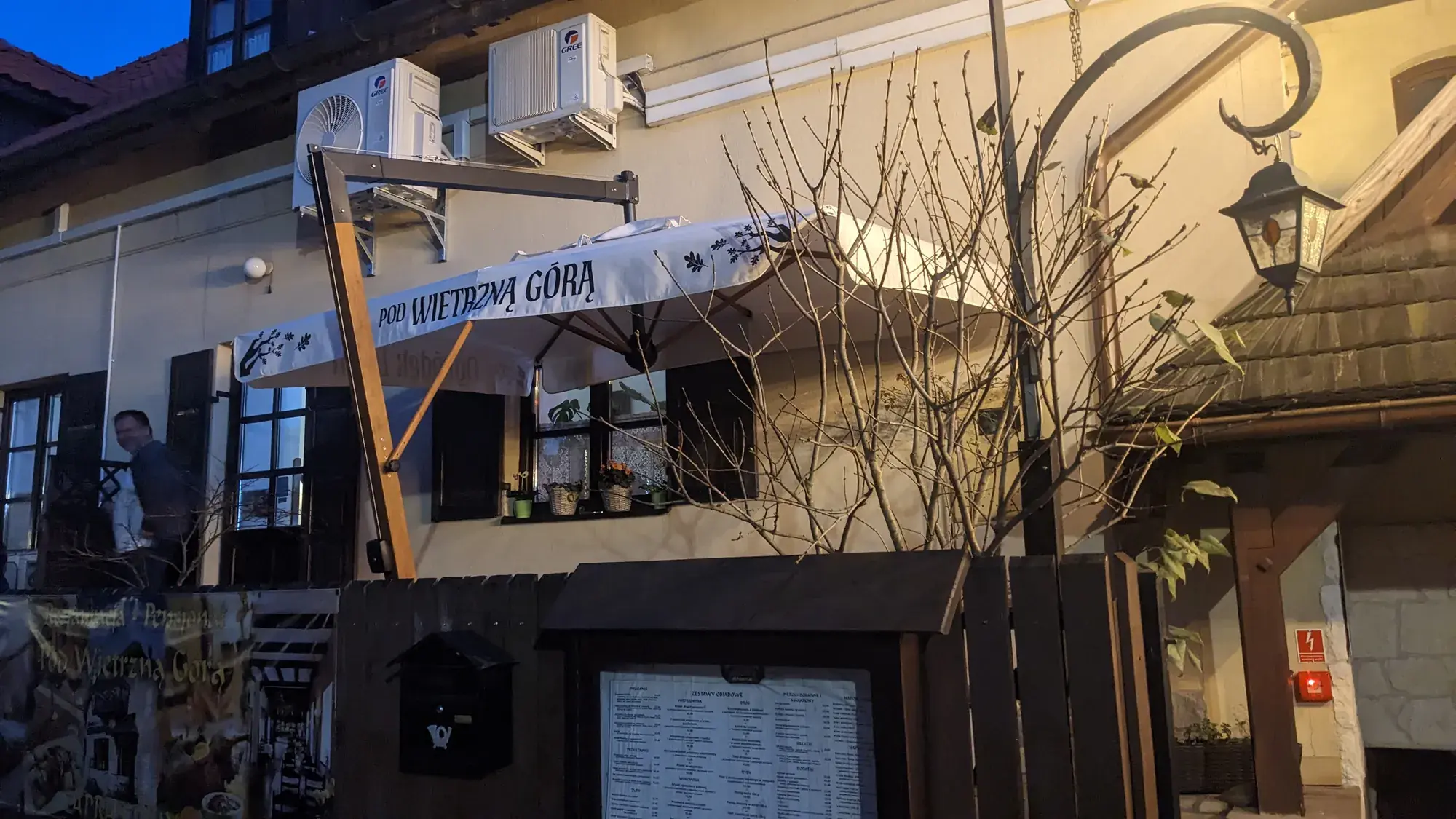 Slunečník s potiskem „Pod Wietrzną Górą“ u vchodu do restaurace v Kazimierzi Dolném