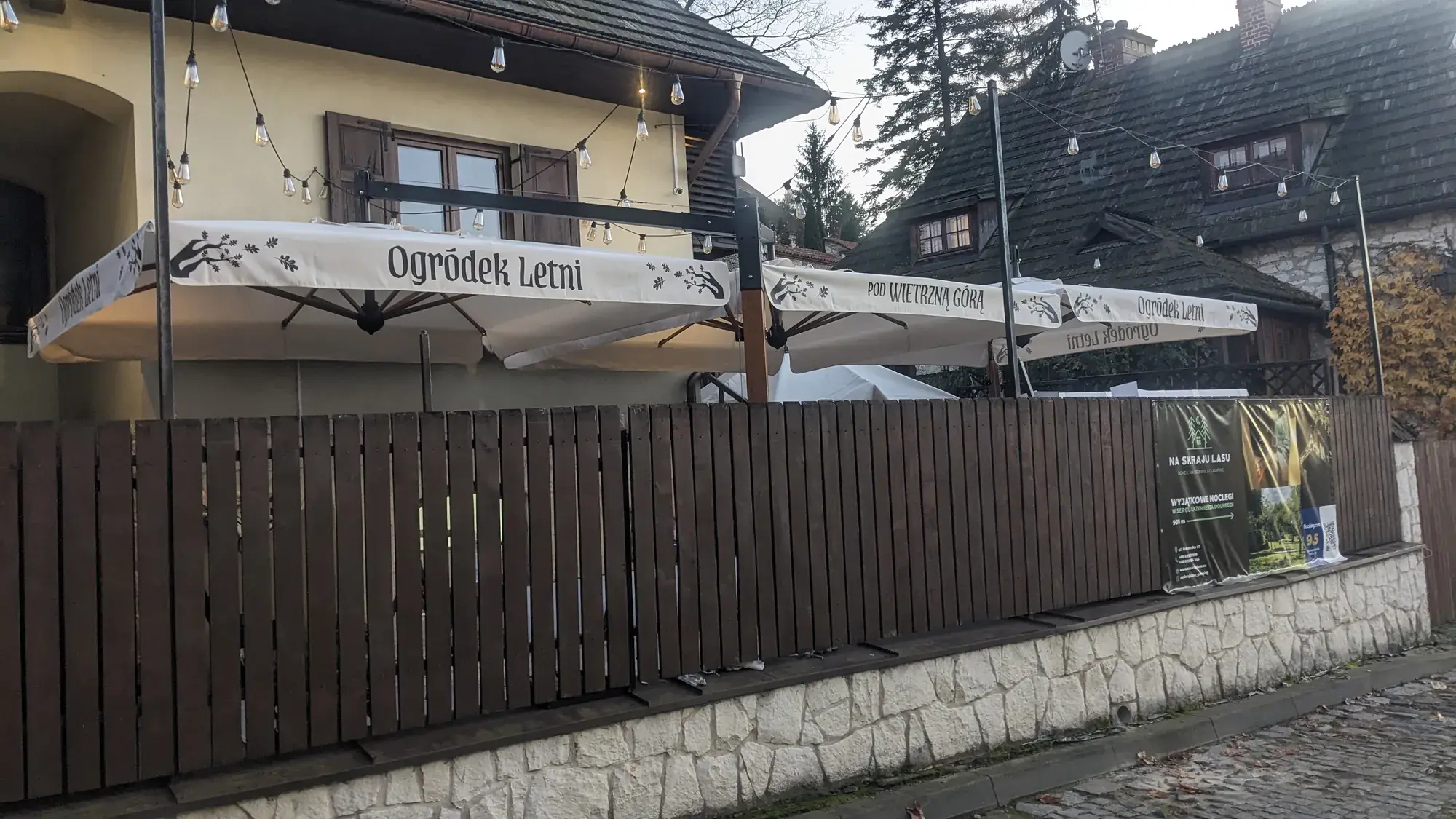 Slunečníky s nápisem „Ogródek Letni“ nad dřevěným plotem restaurace